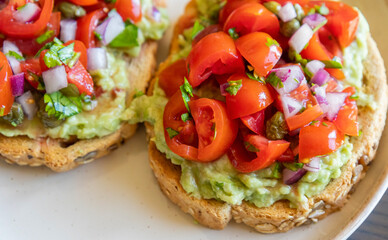 Close-up of fresh avocado toast topped with sliced tomatoes, capers, and parsley, served on a white plate. The dish looks vibrant and delicious, perfect for a healthy breakfast 