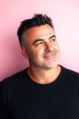 Fototapeta premium Fashionable men's high and tight haircut - midlife white man with black hair. A radiant and poised man in a professional portrait. Artwork design of style for aging men. Pink solid background.