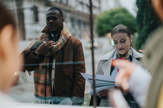 Urban people exchange ideas and review documents outdoors. Captured in a modern, business-oriented setting, the mood reflects collaboration and partnership in an urban environment.