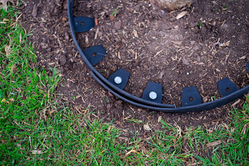 Close-up galvanized spike pierce through no-dig recycled black plastic landscape edging roll to form tight circle around ring to protect trunk, wood chips bedding materials guard fruit tree care