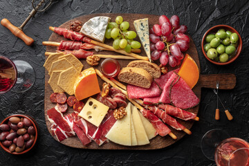 Antipasti or tapas. Charcuterie and cheese platter with wine, shot from above on a black table. Italian or Spanish food and drinks