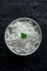 White rice, cooked. A bowl of boiled long grain rice, with fresh parsley leaves, on a black slate background, shot from the top