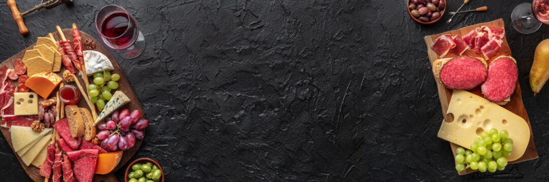 Antipasti or tapas panorama. Charcuterie and cheese board with wine, banner design for a restaurant menu, top shot with copy space