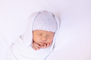 a newborn baby sleeps sweetly in a diaper in a bunny hat with ears on a white background, a place for text