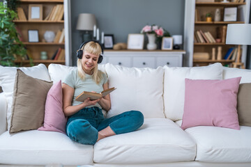 Obraz premium Young woman sitting at home reading a psychology book, working on herself and her mental health after a stressful situation. Female read book that her psychotherapist recommended to her after stress.