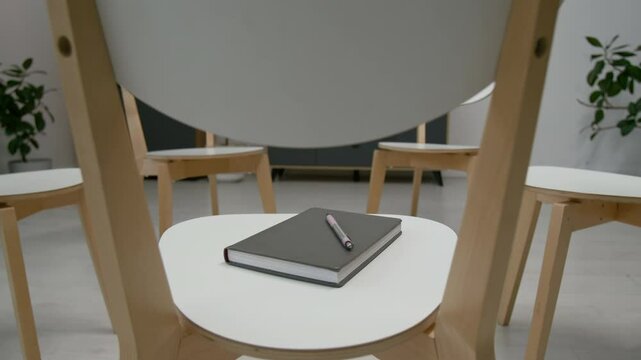 Close-up no people shot of closed notebook and pen on chair in minimalist group therapy room