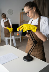 Female professional cleaners wiping desk lamp in living room. team of janitors from cleaning...