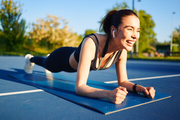 Young sporty woman doing plank exercise outdoors on fitness mat