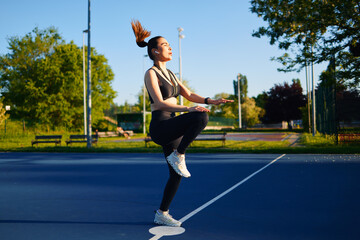 Fit woman doing high knees cardio workout listening music with wireless earphones in urban park