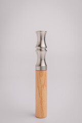 Close-up of a modern duck call made from stainless steel and wood, displayed upright on a white...