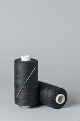 Black thread spools with needle close-up on white background with copy space for text