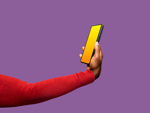 Outstretched Black African hand in red long sleeves body con sweater holding mobile phone with blank yellow screen isolated on purple background. Lift raise showing Three quarter view