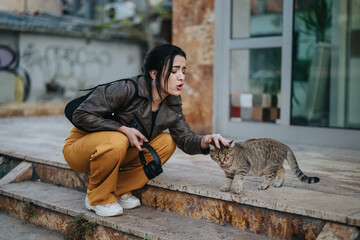 A woman wearing casual clothing kneeling to pet a cat on the street, showcasing a curious...