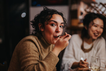 Friends are seated inside a warm and inviting restaurant, sharing food, laughter, and conversation. The atmosphere is relaxed and friendly, emphasizing enjoyment of good company and delicious dining.