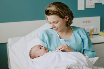 Mother holding newborn baby while smiling in hospital room. Bonding moment between mother and baby...