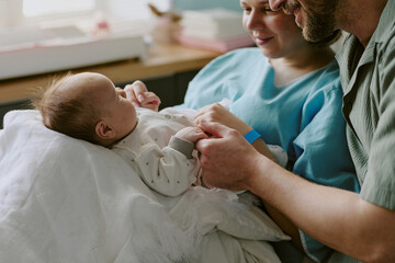 Parents holding newborn baby wrapped in white blanket while sharing a tender moment. Family...