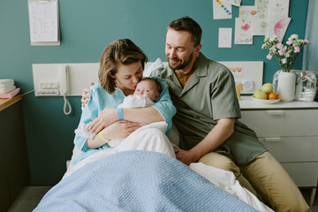 Young parents holding newborn baby in hospital room, smiling and bonding as a family. Caring mother...