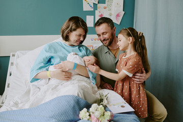 Happy family welcoming newborn baby in hospital room with mother, father, and daughter. Joyful...
