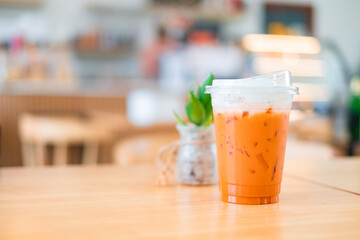 Ice Thai tea in clear plastic cup famous beverage drink traditional on wooden table in nature cafe, copy space