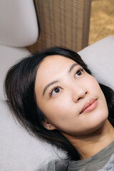 Southeast Asian woman with long eyelash lying on pillow looking relaxed and thoughtful in beauty...