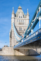 Obraz premium Tower Bridge stands majestically over the River Thames in London, showcasing its iconic architecture under a clear blue sky. The intricate design features both stone and metal elements.