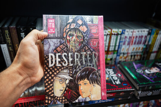 Hand holding a manga book in a comic store with colorful shelves. Deserter by Junji Ito