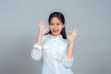 Portrait of a young woman smiling confidently while showing double OK hand signs. Her playful...