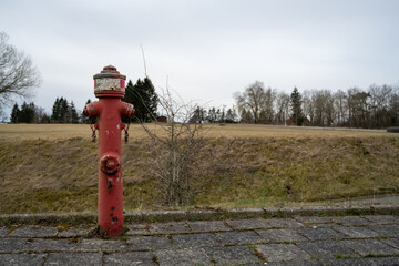 A red fire hydrant is sitting on the sidewalk in front of a grassy field
