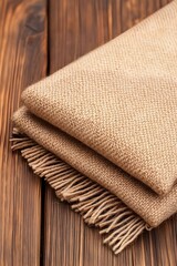 A beige, folded woolen throw blanket with fringe rests on a dark wood surface