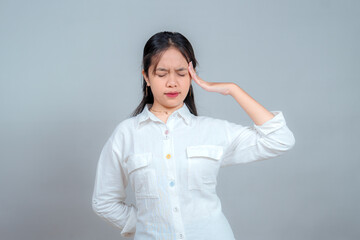 Portrait of an Asian woman with closed eyes and pained facial expression, holding her head in...