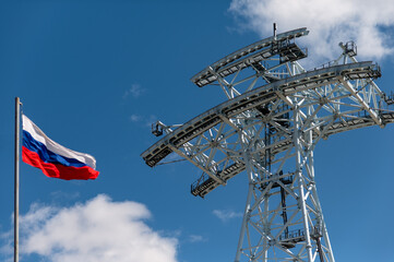 Tower of the cable car under construction between Russia and China. The Russian flag in the foreground is out of focus. View from below. Blue sky with clouds. Sunny day. no people,