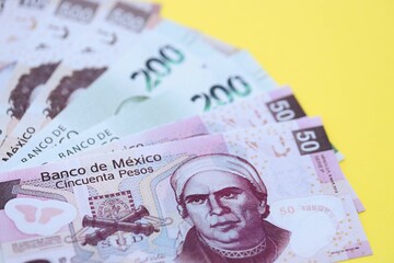 Mexican pesos money bills in big amount lies on yellow color table close up