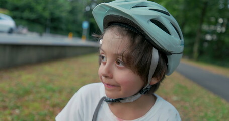 Boy sitting cross-legged on a skateboard with protective gear, looking thoughtful, wearing a...