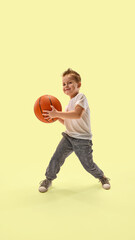 Smiling boy with spiked hair, dressed sportswear, holds basketball ready to play confidently...