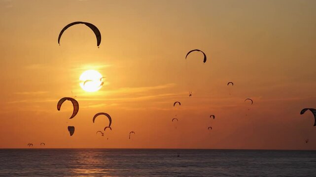 Kiteboarding silhouettes at sunset over water.