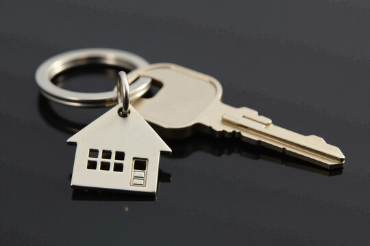 Metallic house-shaped keychain gold key symbolizing homeownership against dark background