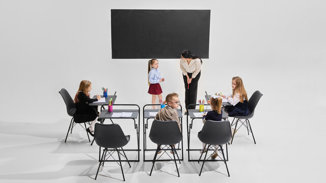 Student presenting in front of classroom while teacher listens kindly, classmates take notes. Student engagement, school learning, confidence building, primary education, classroom story time concept.