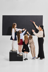 Obraz premium Children and teacher standing near blackboard, girl pointing upward while others observe. Concept of collaboration, team learning, curiosity, child education, academic discovery, growth mindset.