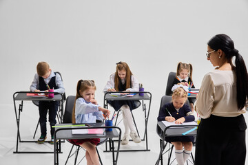 Primary school students concentrating on homework with pencils and notebooks while teacher observes. Concept of quiet study time, writing skills, education, personal growth, focused learning.