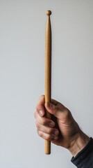 Hand holding a wooden drumstick on a white background. Suitable for music themes, teaching drumming.