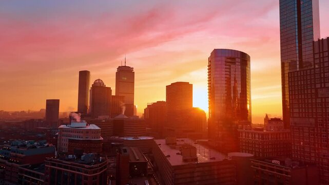Pink light coloring the scenery of beautiful Boston, Massachusetts, USA. Smoke rises from the pipes of the high-rise buildings. Sunset time city aerial.