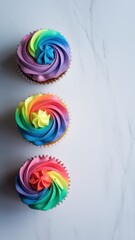 Three vibrant rainbow swirl cupcakes on clean white background