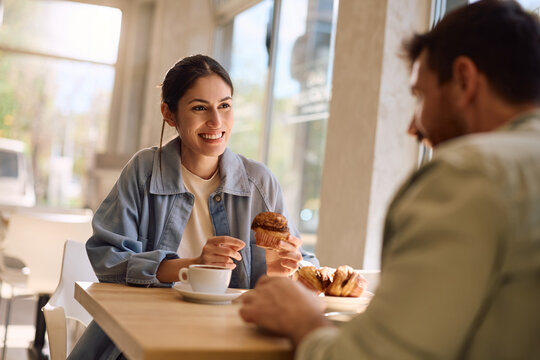 Happy woman talking to her boyfriend while eating cupcake at bakery shop.