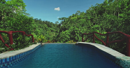 Luxury infinity swimming pool overlooks a vibrant tropical jungle valley forest, offering breathtaking views of nature beauty and creating a serene escape. Exotic travel vacation getaway. Drone flight