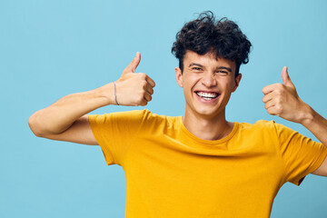 happy young man showing thumbs up in a cheerful blue background, expressing positivity and joy with...