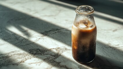 Chilled iced coffee in a glass bottle with morning light and shadows
