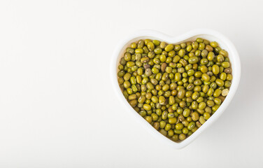 White heart shape bowl full of mung beans or dal on white background isolated, top view with copy space