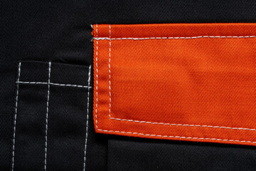 Orange flap of black pants pocket, closeup. Background and texture of fabric