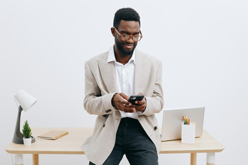 Professional young African American man in smart casual clothing using smartphone in modern office setting with minimalist decor and natural light, representing workplace communication and technology
