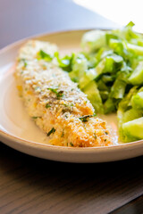 Close-up of a baked breaded salmon fillet served with a simple green salad in a dish. The salmon has a golden, crispy crust and is paired with fresh greens